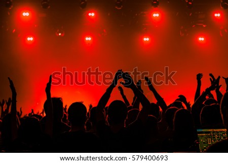 Silhouettes of people in a bright in the pop rock concert in front of the stage. Hands with gesture Horns. That rocks. Party in a club. Red background.