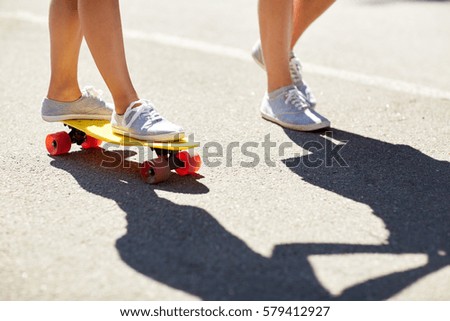 summer, extreme sport and people concept - feet of teenage couple riding short modern cruiser skateboard on road