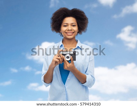 people and photography portrait concept - happy african american young woman with film camera over blue sky and clouds background