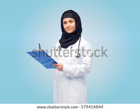 medicine, healthcare and people concept - smiling muslim female doctor wearing hijab and white coat with clipboard and stethoscope over blue background