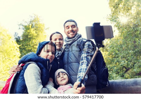 technology, travel, tourism, hike and people concept - happy family with backpacks taking picture by smartphone on selfie stick and hiking