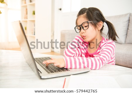 elementary young asian girl feel bored to using her computer and reading book at the table in the living room at home. family activity concept.