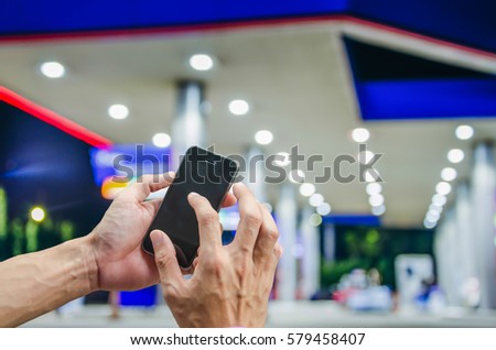 Hand using smartphone for internet online on Blur image of a gas station at night backgrond