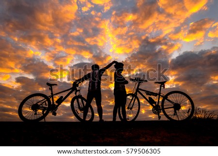 cyclist and Bicycle silhouettes on the dark background of sunrise and  dark clouds. 