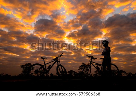 cyclist and Bicycle silhouettes on the dark background of sunrise and  dark clouds. 
