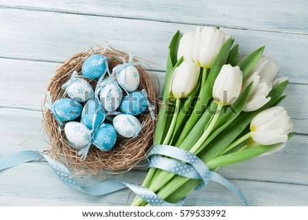 Easter eggs and white tulips on wooden background. Top view