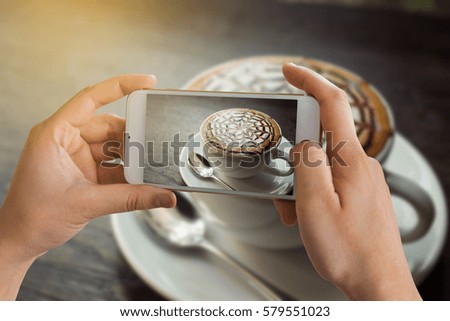Woman taking a picture of a coffee cup with her smart phone while sitting at a coffee shop.