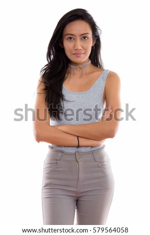 Studio shot of young beautiful Asian woman standing with arms crossed