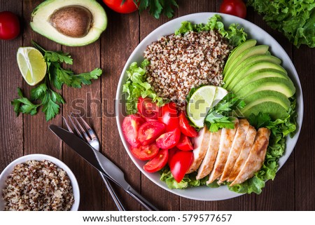 Healthy salad plate with quinoa, cherry tomatoes, chicken, avocado, lime and mixed greens, lettuce, parsley on wooden background top view. Food and health. Superfood meal.