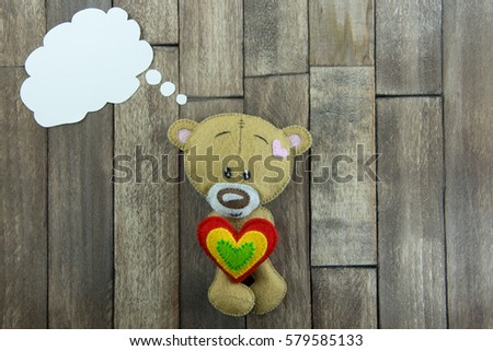 Valentines Day postcard. Teddy Bear and colourful heart and free space for greetings in thought bubble on a wooden background.