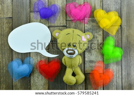Valentines Day postcard. Teddy Bear and colourful hearts and free space for greetings in speech bubble on a wooden background.