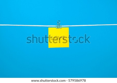 Yellow paper note on clothesline with text Love over colorful background