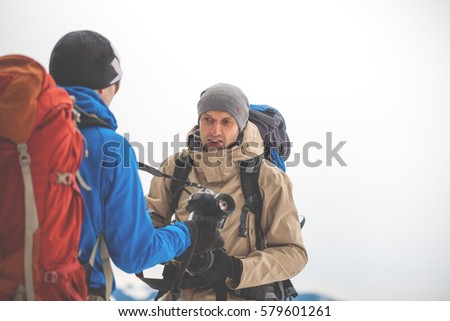 Two photographers with backpacks show each other the cameras during winter hike in the mountains, mountaineer photographs in the mountains in winter, tourist in mountains with the camera.