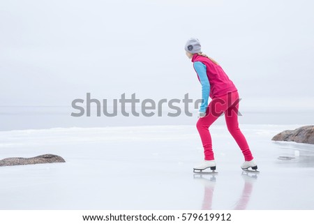Woman with white skates skating and looking around on the ice area at the seashore in winter day. Foggy air. In front of view opens infinity. Enjoying weekends activities outdoor in cold weather. 
