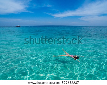 Aerial view of young brunette woman swimming in the transparent turquoise sea at the tropical island. Top view of slim lady relaxing on her holidays in Thailand, Phuket, Andaman sea.