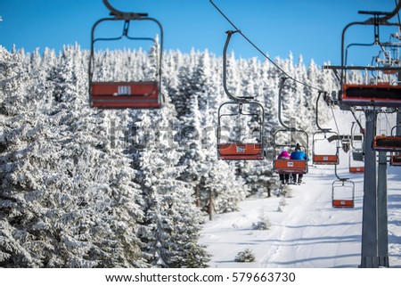 Ski lift with skiers being carried up the hill on a lovely, sunny winter day