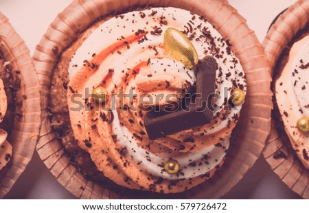 Vanilla cupcakes with orange and white creamcheese and chocolate decor. Toned.