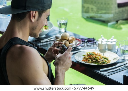Side view of a handsome young man taking a photo of his food in the restaurant. Horizontal indoors shot.