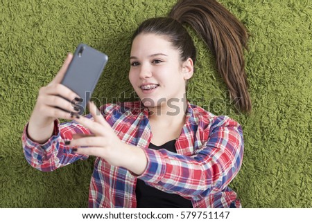 Young teenage girl lying on the floor taking selfie