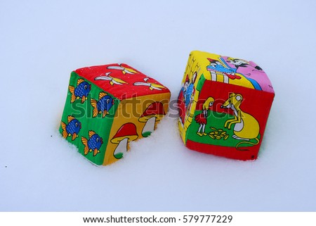 Colored foam and fabric cubes with pictures of fruits and tales of heroes, lies on a white dry snow