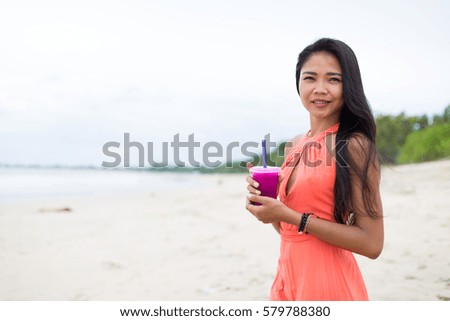 Young girl drinking a fruit smoothie on the beach in Bali, Indonesia