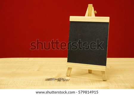 Mini chalkboard with pile of paper clips on wooden table over red background