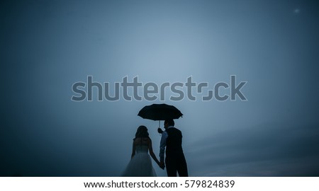 Groom holding an umbrella over the bride on a background cloudy dark blue summer sky