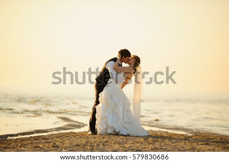 bride and groom walking on the sand at sunset Royalty-Free Stock Photo #579830686