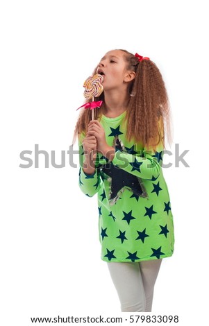 Young girl with long hair in a green tunic with a big candy on a stick posing on a white background in studio