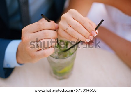 man and woman holding cocktail with lime and ice. Hands holding tube on hand rings bride and groom