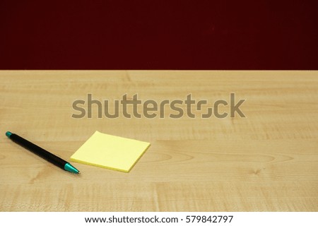 Pen and yellow paper notepad on wooden table over red wall background