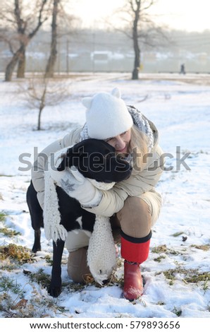 Woman in winter clothes covering beautiful black dog with woolen scarf on winter day