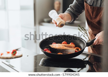 Cropped picture of young amazing woman standing in kitchen while cooking fish