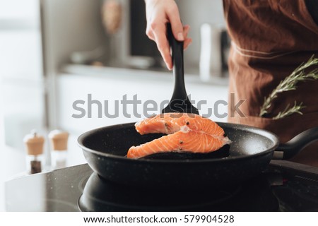 Cropped picture of young lady standing in kitchen while cooking fish.
