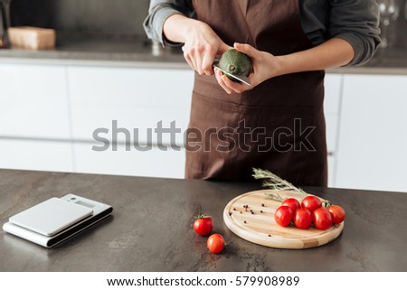Cropped picture of young woman standing in kitchen cut the tomatoes and avocado.