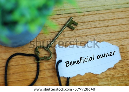 Key and torn paper with text beneficial owner on wooden background Royalty-Free Stock Photo #579928648