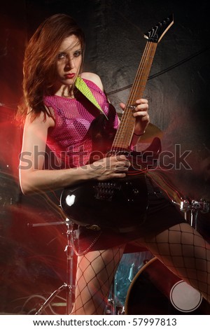 Photo of a female guitarist playing on a stage. Shot with strobes and slow shutter speed to create lighting atmosphere and blur effects. Slight motion blur on performer.