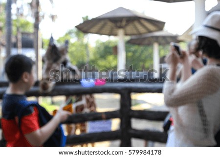 Abstract blur tourists feeding some food to giraffe and taking photo  in open zoo.