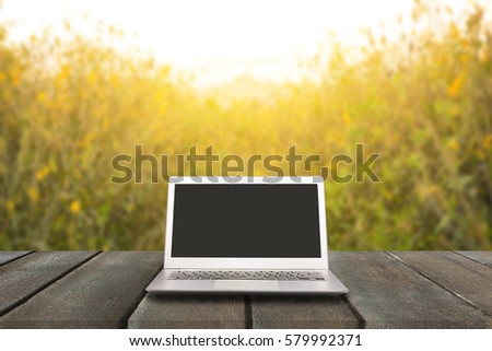 Laptop with blank screen on wooden table with absract yellow flower and flare light background, can used for display or montage your products