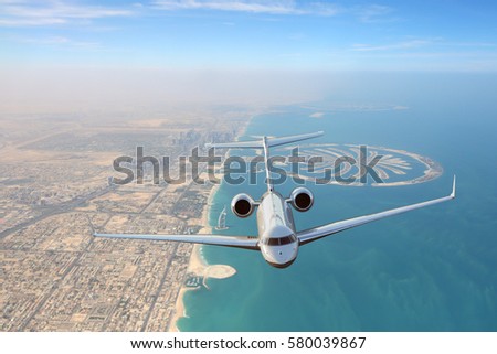 Business jet airplane flying over Dubai city and sea coastline. Royalty-Free Stock Photo #580039867