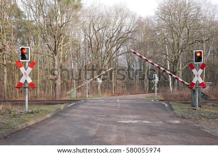 Barriers coming down on a wooded rural level crossing with flashing red warning lights to stop motorists crossing the railway line as a train is due to come through