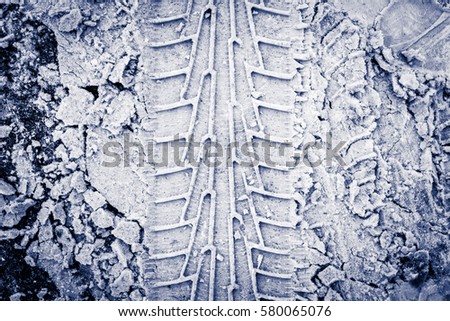 Vertical traces of car tires in the snow on the asphalt. Close up view from above, image vignetting and the blue toning