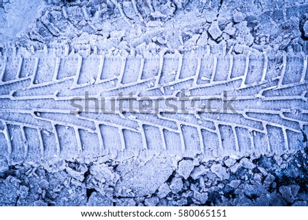 Parallel traces of car tires in the snow on the asphalt. Close up view from above, image vignetting and the blue toning