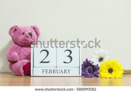 Closeup surface white wooden calendar with black 23 february word on brown wood desk and cream color wallpaper in room textured background with copy space in selective focus at the calendar