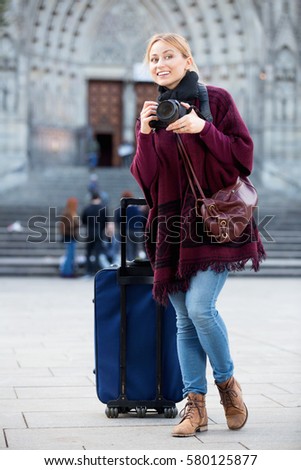 Young cheerful smiling girl taking picture with camera in the town 