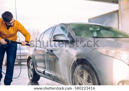 Shot of a handsome male washing his car with water outdoors.