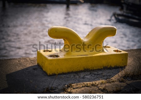 Horizontally oriented picture of port pier with yellow mooring bollard.