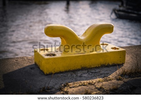 Horizontally oriented picture of port pier with yellow mooring bollard.