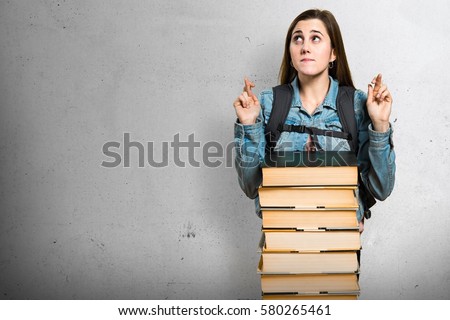 Teen student girl with a lot of books and with her fingers crossing