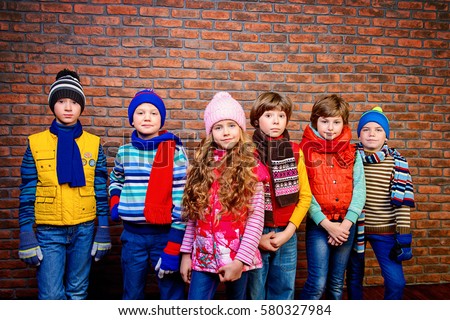 Group of happy joyful children posing together at studio by the brick wall. Kid's fashion. Winter clothes.